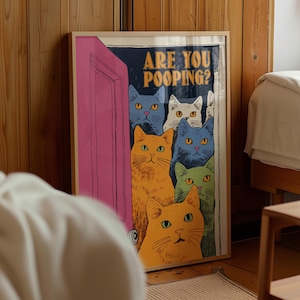 May include: A framed rectangular wall art print featuring a pink door slightly ajar with several colorful cats peering through the opening. The text ARE YOU POOPING? is printed in yellow at the top. The cats are depicted in shades of blue, orange, white, and green.
