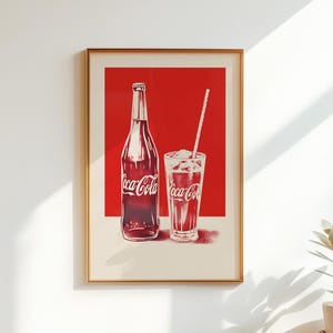 May include: A framed wall art print featuring a red background with a white illustration of a glass Coca-Cola bottle and a glass of Coca-Cola with ice and a straw. The Coca-Cola logo is clearly visible on both the bottle and the glass.