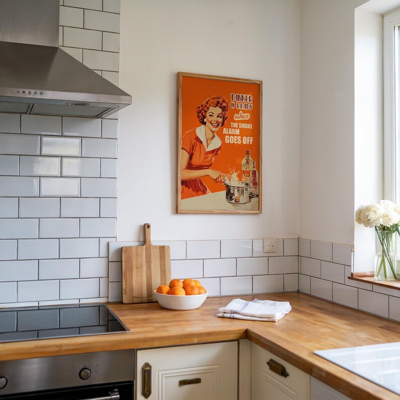 Retro style poster of a smiling housewife in an orange kitchen with a funny quote. Fun kitchen print in a 50s aesthetic for nostalgic decor.