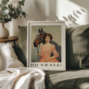 Vintage-style poster of a woman in a pink dress standing beside a horse, styled as equestrian wall art with country chic art and western decor charm, text reads “HOLD YOUR HORSES”