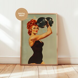 Vintage 1950s style pin-up girl art print featuring a strong woman with red hair lifting a heavy black dumbbell overhead. Retro fitness wall art showing a muscular woman in a black swimsuit, perfect for a vintage home gym decor, garage art, or mid-century modern aesthetic.