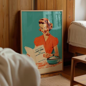 May include: A framed poster featuring a retro-style illustration of a person with red hair wearing an orange shirt, reading a book titled How to turn I CAN'T COOK into I CAN'T BELIEVE I MADE THIS! The Art of Microwaving, next to a teal bowl.