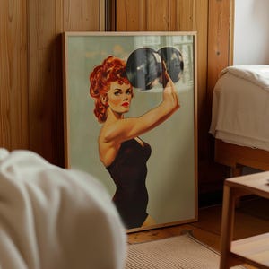Vintage 1950s style pin-up girl art print featuring a strong woman with red hair lifting a heavy black dumbbell overhead. Retro fitness wall art showing a muscular woman in a black swimsuit, perfect for a vintage home gym decor, garage art, or mid-century modern aesthetic.