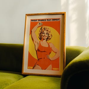Retro gym art featuring an 80s style woman in an orange bodysuit flexing. Vibrant yellow sun background with the text Sweat Sparkle Slay Repeat. Maximalist dopamine decor for home gym walls.