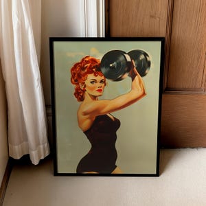 Vintage 1950s style pin-up girl art print featuring a strong woman with red hair lifting a heavy black dumbbell overhead. Retro fitness wall art showing a muscular woman in a black swimsuit, perfect for a vintage home gym decor, garage art, or mid-century modern aesthetic.