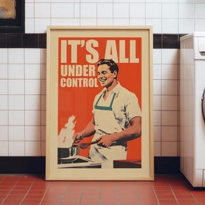 May include: A framed poster featuring a smiling person wearing an apron while cooking at a stove with flames rising from a pan. The orange background includes the bold white text IT'S ALL UNDER CONTROL. The poster has a light wood frame.