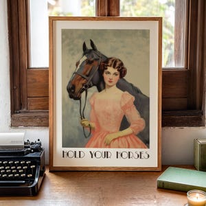 Vintage-style poster of a woman in a pink dress standing beside a horse, styled as equestrian wall art with country chic art and western decor charm, text reads “HOLD YOUR HORSES”