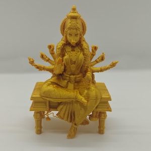 May include: A golden-colored statue of a multi-armed deity seated on a small table. The figure is adorned with intricate details, including a headdress and jewelry. The statue's pose is serene, with multiple arms gracefully positioned.