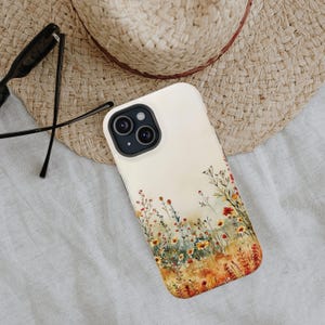 May include: A white phone case with a watercolor design of a field of wildflowers in shades of yellow, orange, and red. The case has a camera lens cutout and a white background.