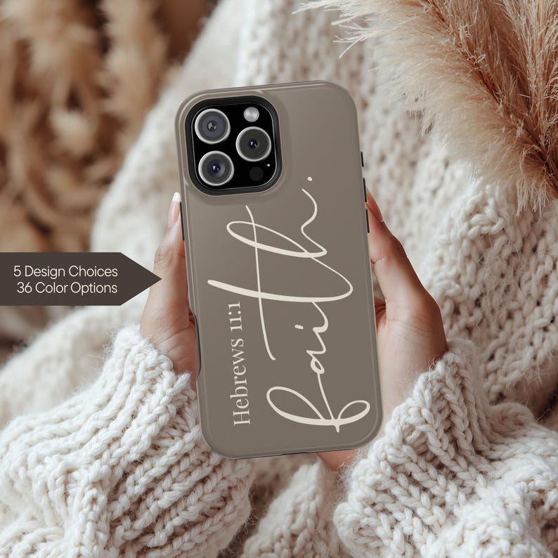 May include: A taupe phone case with the word "Faith" in a cursive font. The text "Hebrews 11:1" is below the word "Faith". The case is held in front of a cream-colored sweater. The text "5 Design Choices 36 Color Options" is on the left.