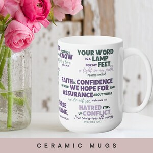 May include: A white ceramic mug featuring various Bible verses printed in purple and green text. The visible text includes Psalms 119:105, Hebrews 11:1, Proverbs 10:12, 1 John 4:8, and Matthew 18:20. The mug has a curved handle and a smooth finish.