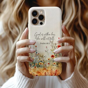May include: A cream-colored phone case featuring a floral design with red, yellow, and orange flowers. The case has the text "God is within her, she will not fall. Psalm 46:5" in black script.