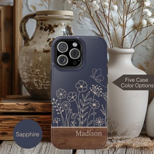 May include: A navy blue phone case with a floral design and a wooden bottom. The case has the name "Madison" printed on the wooden section. The text "Five Case Color Options" is also visible.