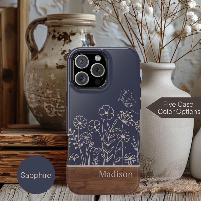 May include: A navy blue phone case with a floral design and a wooden bottom. The case has the name "Madison" printed on the wooden section. The text "Five Case Color Options" is also visible.