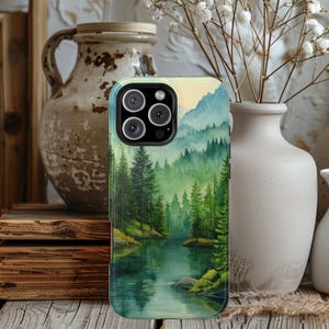 May include: A phone case featuring a watercolor landscape of a forest and lake. The design includes green trees, blue mountains, and a reflective body of water. The case has a glossy finish and a camera cutout.