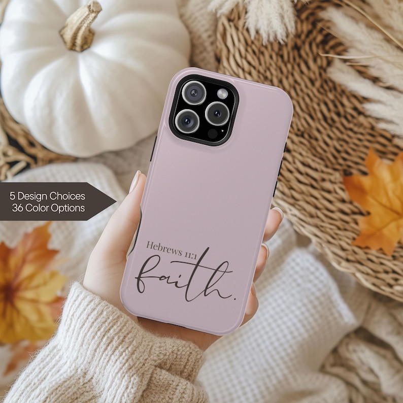 May include: A light purple phone case with the word "faith" in cursive, and the text "Hebrews 11:1". The case is held in a hand, with a background of fall-themed decor. The text "5 Design Choices 36 Color Options" is also visible.