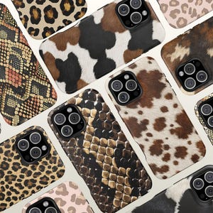 May include: A collection of smartphone cases featuring various animal print patterns including leopard spots, snakeskin textures, and cow hide patches in shades of brown, black, white, and tan, each with a cutout for a triple-lens camera system.