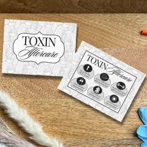 May include: A wooden tray containing various items for a beauty treatment. There are two small bottles, three syringes, a pair of blue gloves, and two cards with the text "TOXIN Aftercare". There is also a bunch of dried pampas grass.