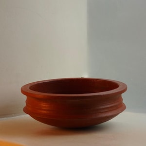 Puede incluir: Un cuenco de terracota sobre una superficie blanca con una pared blanca en el fondo.