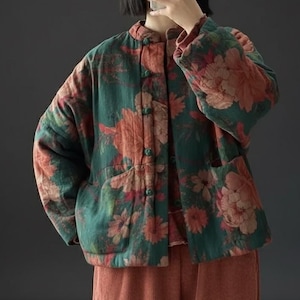 Könnte beinhalten: Grüne Jacke mit floralem Print, Stehkragen und Knopfverschluss. Die Jacke hat zwei Vordertaschen und wird mit rostfarbenen Cordhosen kombiniert. Das Blumenmuster zeigt große, stilisierte Blumen in Rot-, Orange- und Rosatönen.