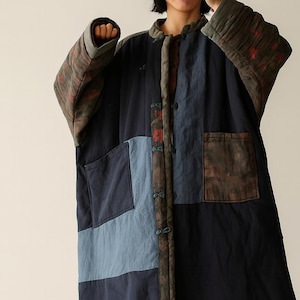 Puede incluir: Un abrigo largo de patchwork en azul marino, azul claro y marrón. El abrigo presenta grandes bolsillos y un diseño acolchado en las mangas. El abrigo tiene una parte delantera abotonada y una estética artística única. Las mangas tienen un diseño acolchado con acentos rojos.