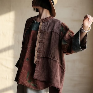 Puede incluir: Chaqueta de estilo patchwork en tonos marrón, rojo y verde. La chaqueta tiene cuello mandarín y cierres de botón. Las mangas tienen un ribete verde oscuro en contraste. La prenda parece estar hecha de una tela texturizada.