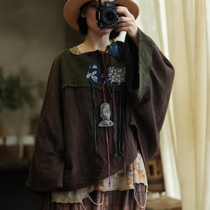 May include: A brown, long-sleeved top with a patchwork design. The top features a green yoke, blue and white patterned patches, and a decorative pendant. The sleeves are wide and flowing, and the overall style is bohemian.