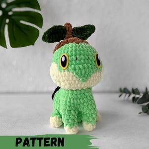 May include: Green crocheted plush toy with a brown head and a green leafy crown. The toy has large yellow eyes and a small brown nose.