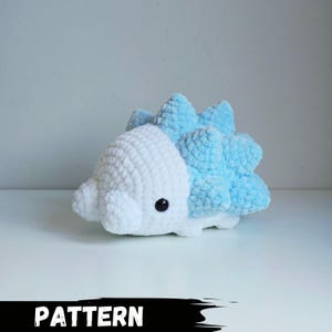 Könnte beinhalten: Ein handgefertigtes Plüschtier in Form einer kleinen, stilisierten Kreatur. Das Spielzeug ist überwiegend weiß mit hellblauen Akzenten auf dem Rücken. Es hat ein schwarzes Knopfauge und eine abgerundete Form. Das Wort "PATTERN" ist unten aufgedruckt.