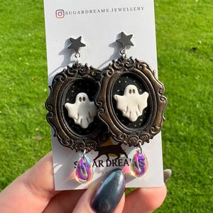Op de afbeelding: Een paar Halloween-oorbellen. Elke oorbel heeft een witte geest in een bronzen lijst, met een ster erboven. Iridescent traanvormige bedels hangen eronder. De oorbellen worden getoond op een witte kaart met de tekst "SUGAR DREAMS JEWELLERY".