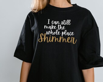 May include: Black t-shirt with the text "I can still make the whole place shimmer" in white and gold lettering.