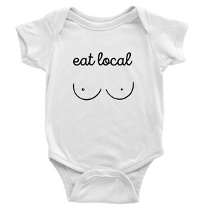 Puede incluir: Body de bebé blanco con la frase "eat local" en escritura negra sobre un sencillo dibujo lineal negro de pechos. El body tiene mangas cortas y corchetes en la parte inferior.