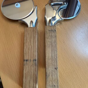 May include: Two silver pizza cutters with wooden handles. The handles are made from reclaimed oak barrels.