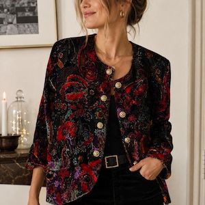 Peut inclure: Une veste en velours à manches longues arborant un motif floral et cachemire multicolore dans des tons de rouge, violet et noir. La veste présente une encolure ronde, un ourlet droit et une fermeture frontale avec cinq boutons dorés.