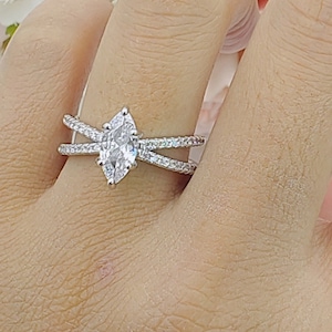 Op de afbeelding: Een zilveren ring met een marquise-vormige diamant en een dubbele band ontwerp. De ring is bezet met kleinere diamanten rond de middelste steen.