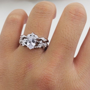 Op de afbeelding: Een zilveren ring met een peervormige, heldere steen omgeven door kleinere heldere stenen in een bladontwerp.