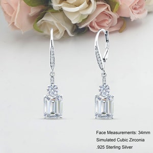 May include: Silver dangle earrings with a large emerald-cut cubic zirconia stone and smaller round cubic zirconia stones. Face Measurements: 34mm. Simulated Cubic Zirconia. 925 Sterling Silver.