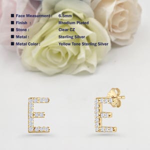 May include: A pair of gold-tone sterling silver earrings with a clear CZ letter 'E' design. The earrings are 6.5mm in size and have a rhodium plated finish.