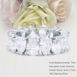 May include: A silver eternity band ring with a row of pear-shaped simulated cubic zirconia stones. The ring is 7mm wide and the center stone is 5mm by 7mm. The ring is made of .925 sterling silver.