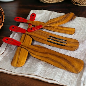 Può includere: Set di quattro spatole in legno con manici rossi. Le spatole hanno una finitura in legno naturale e sono progettate per cucinare e servire.