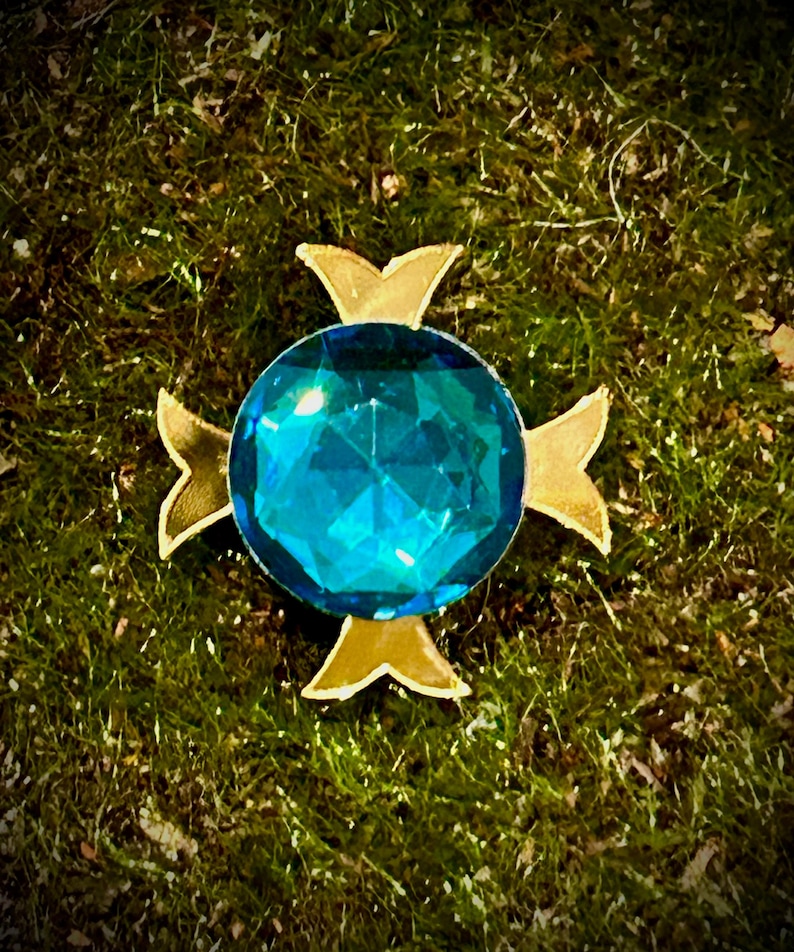 May include: A blue gemstone set in a gold four-pointed star design.
