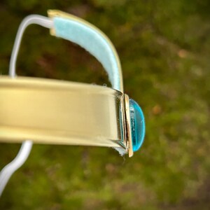 May include: A gold bangle bracelet with a turquoise blue cabochon stone set in the center.
