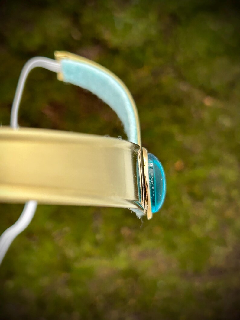 May include: A gold bangle bracelet with a turquoise blue cabochon stone set in the center.