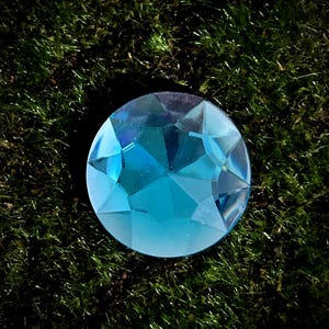 Op de afbeelding: Een grote, gefacetteerde, blauwe edelsteen met een hoge glans. De edelsteen is rond en heeft een heldere, glazige uitstraling.