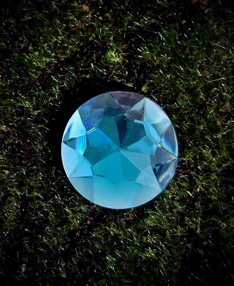 Op de afbeelding: Een grote, gefacetteerde, blauwe edelsteen met een hoge glans. De edelsteen is rond en heeft een heldere, glazige uitstraling.