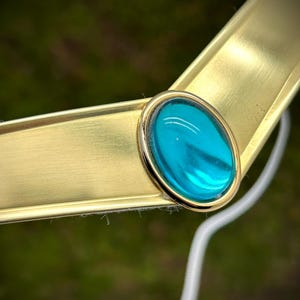 May include: A gold-colored metal headband with a teal blue oval-shaped gem in the center.
