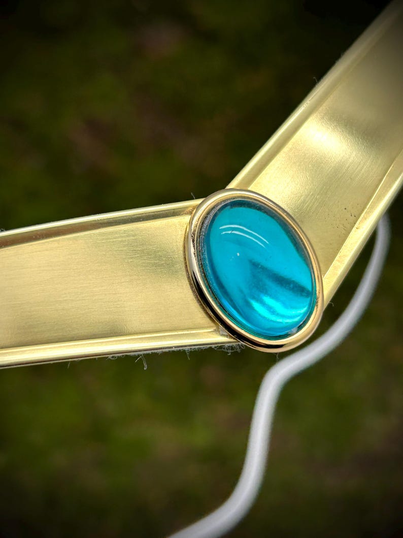 May include: A gold-colored metal headband with a teal blue oval-shaped gem in the center.