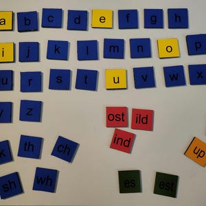 May include: Alphabet and word building tiles. Blue and yellow square tiles with letters of the alphabet, and red, green, and orange tiles with word endings and prefixes. Educational toy for learning to read and spell.