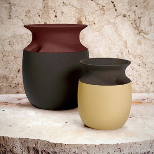 May include: Two ceramic vases with a textured finish. The larger vase is dark grey with a burgundy top, and the smaller vase is beige with a dark brown top. Both vases have a rounded shape and a flared rim.