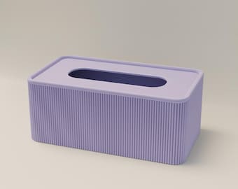 May include: A rectangular tissue box in a soft lavender color. The box has a ridged texture on the sides and a smooth top with an oval opening. The interior of the opening is a darker shade of purple.